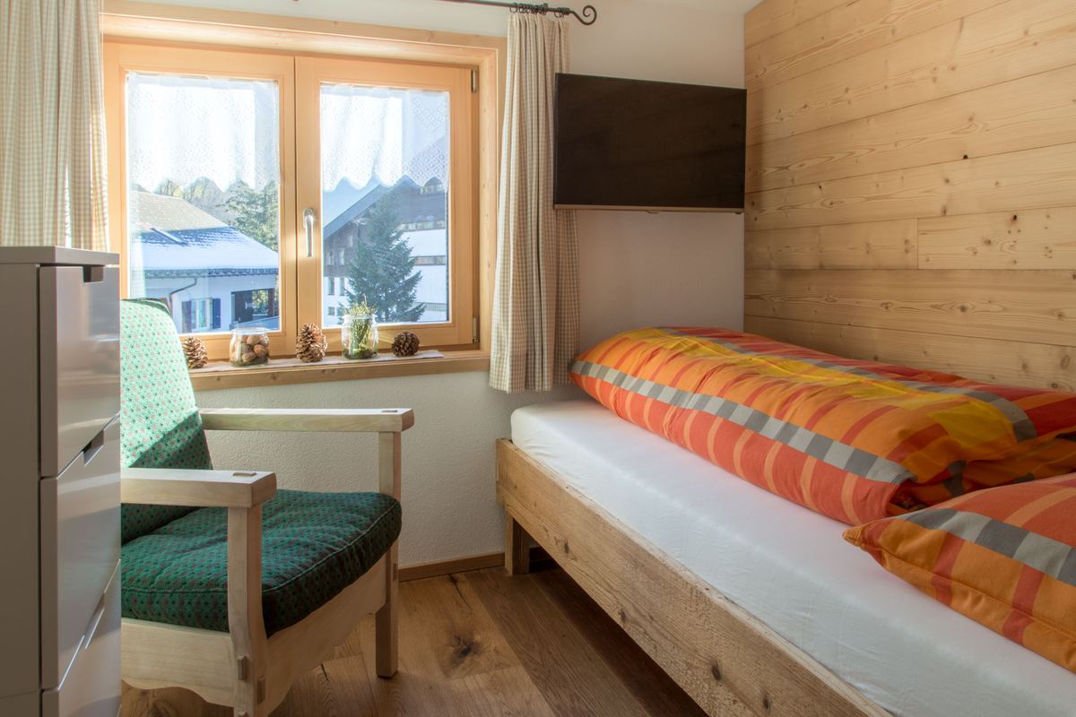 Einzelzimmer mit Bett, Sessel am Fenster und Blick auf die Häuser von Mellau