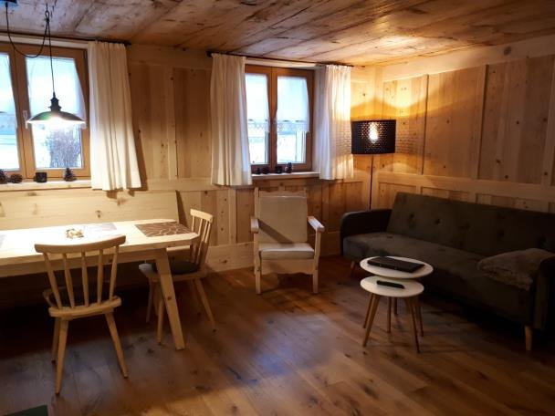 Wohnraum des Appartements Mittagsspitze mit Esstisch, Sessel und Sofa vor Wänden und Decke aus altem Holz